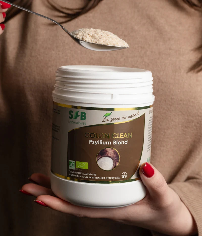 Poudre en sachet blanc dans un pot alimentaire marqué « COLON CLEAN Psyllium Blond » tenu par une main à ongles rouges.